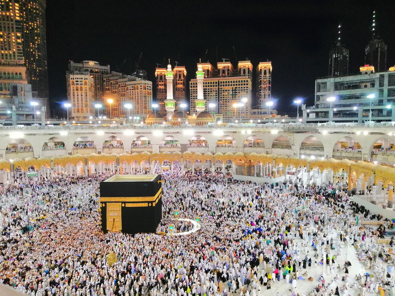 Services Aerial view of the Kaaba surrounded by pilgrims in Makkah at night, showcasing a religious gathering.